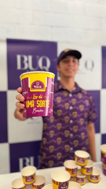 Atendente Trevo segurando balde de açaí em ativação de marca com backdrop corporativo