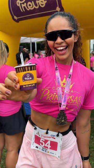 Corredora com medalha segurando copo de açaí Trevo na chegada da corrida